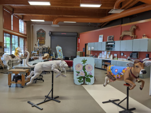 A spacious room with various colorful animal sculptures and art displays, featuring a white dog, a decorated cow, and more.