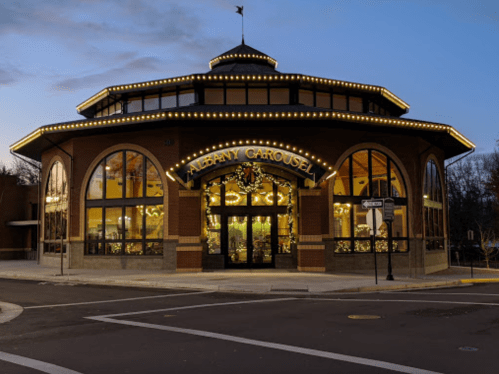 A beautifully lit carousel building at dusk, featuring the sign "Albany Carousel" and decorative lights.