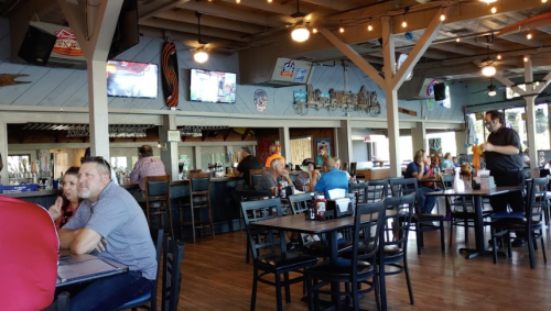 A lively restaurant interior with wooden decor, tables filled with diners, and TVs showing sports in the background.