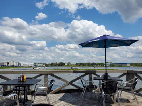 A scenic view of a waterfront with a table and umbrella, surrounded by clouds and greenery.