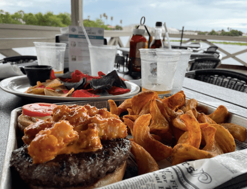 A plate with a burger topped with shrimp, sweet potato fries, and a side of tortilla chips on a restaurant table.