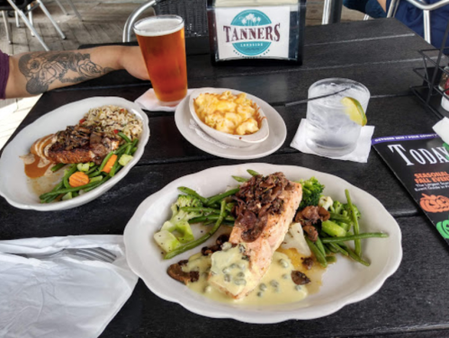 A table with a plate of salmon, green beans, and mashed potatoes, a side of mac and cheese, a beer, and a glass of water.