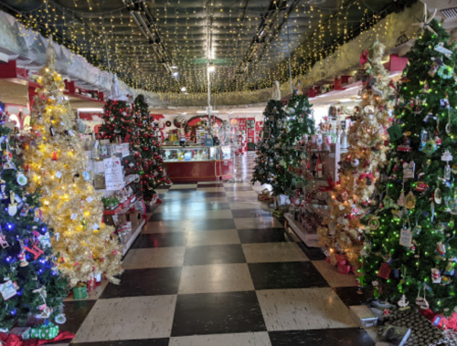 A festive shop interior filled with decorated Christmas trees and twinkling lights, creating a cheerful holiday atmosphere.