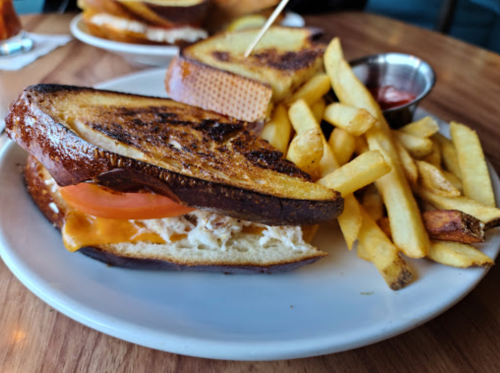 A grilled sandwich with cheese and tomato, served with a side of golden fries and a small cup of ketchup.