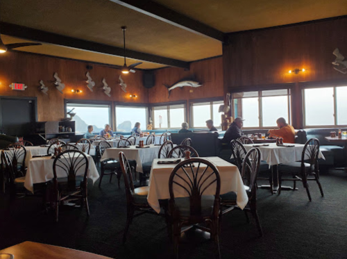 A cozy restaurant interior with wooden decor, tables set for dining, and patrons enjoying their meals by large windows.