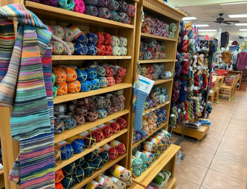 A colorful display of yarn in a craft store, featuring shelves filled with various skeins and a knitted scarf.