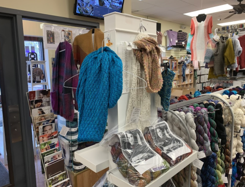 A yarn store display featuring colorful knitted items, yarn skeins, and patterns in a cozy retail environment.