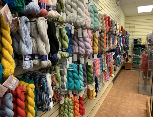 A colorful display of yarn skeins arranged on shelves in a craft store, showcasing various textures and shades.
