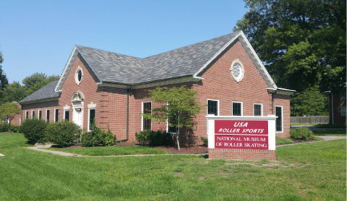 A brick building with a sloped roof, featuring a sign for the National Museum of Roller Skating and green landscaping.