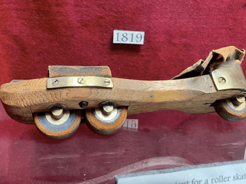 A vintage wooden roller skate model from 1819, featuring metal wheels and a simple design.