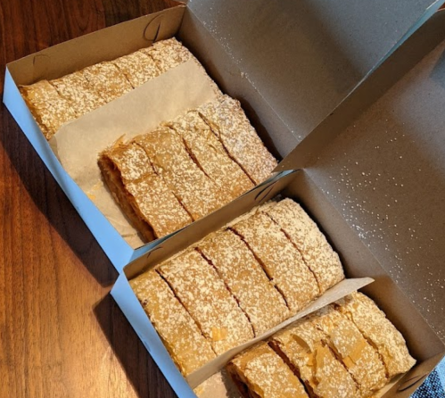 Two boxes of freshly baked strudel, dusted with powdered sugar, neatly sliced and arranged on a wooden table.