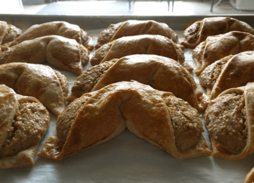 A close-up of freshly baked pastries with a golden-brown crust and a visible filling, arranged on a baking tray.