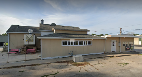 A single-story building with a beige exterior, featuring a flat roof and several windows, set on a cracked concrete surface.