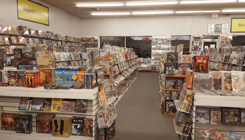 A spacious store aisle filled with shelves of board games and boxed games, neatly organized for browsing.