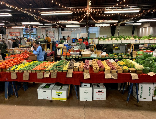 A vibrant farmers market with colorful fruits and vegetables displayed on tables under string lights.
