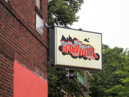 Sign for "The Uptowner Cafe" with a vibrant design, located on a brick building near a traffic signal.