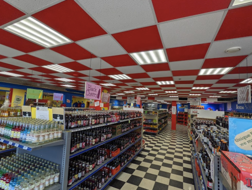 Interior of a colorful store with red and white checkered ceiling, shelves filled with various beverages, and a checkered floor.