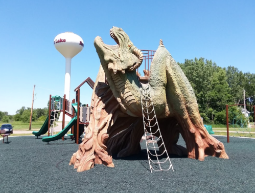 A playground featuring a large dragon climbing structure with a slide and a water tower in the background.