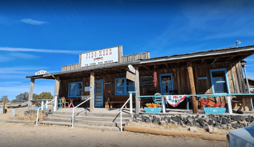 A rustic wooden building with a porch, signs, and colorful decorations, set against a clear blue sky.