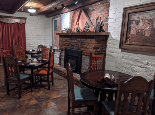 Cozy restaurant interior with wooden tables, chairs, a brick fireplace, and decorative wall art.