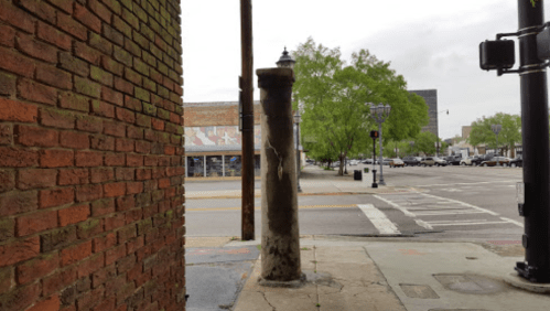 A view of a street corner with a brick wall, a weathered pole, and a traffic light, under a cloudy sky.