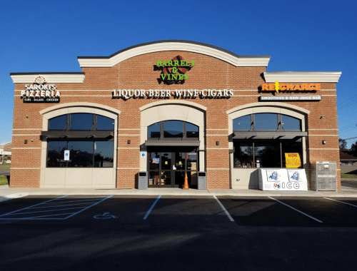 Exterior of a brick building featuring a liquor store, pizzeria, and smoothie shop, with clear signage and parking.