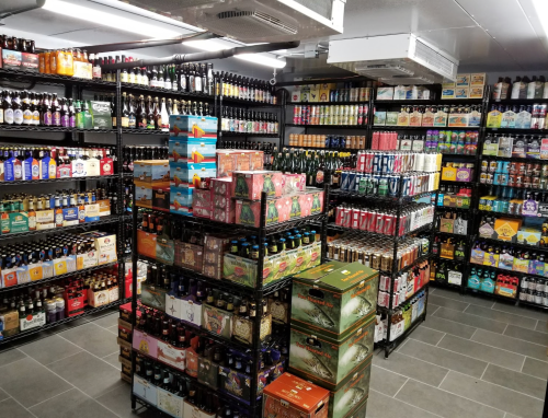 A well-organized beverage store with shelves stacked high with various bottles and boxes of beer and other drinks.