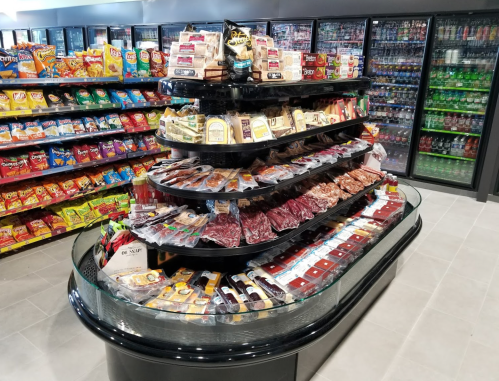 A display case filled with various packaged snacks, meats, and cheeses, surrounded by shelves of chips and drinks.
