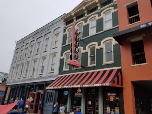 A vintage building with a red and white striped awning, featuring a sign for a burger restaurant, on a cloudy day.