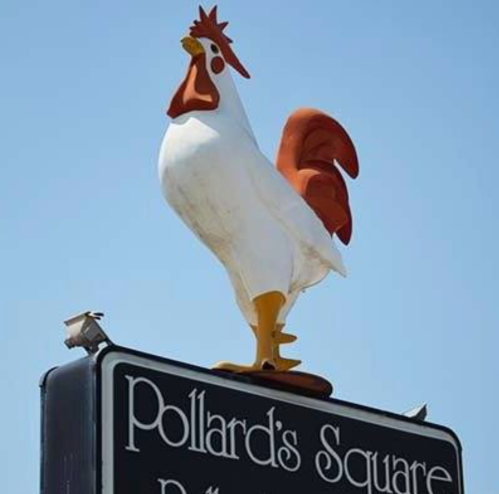 A large, colorful rooster statue atop a sign for Pollard's Square against a clear blue sky.