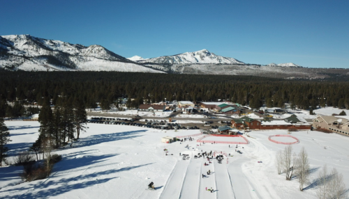 A snowy landscape with mountains in the background, featuring a ski area and people enjoying winter activities.