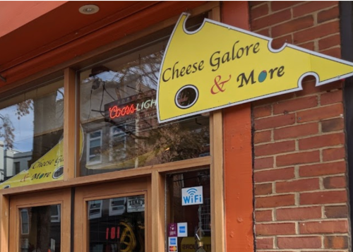 Sign for "Cheese Galore & More" on a brick storefront, featuring a cheese wedge design and WiFi symbol.