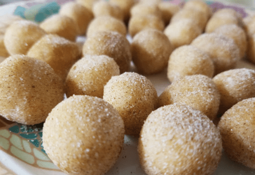 A plate of small, round, golden-brown sweets coated in a fine layer of sugar or powder.