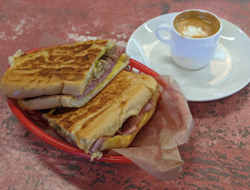 A plate with two toasted sandwiches and a small cup of espresso on a red table.