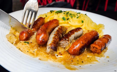 A plate of sausages served with sauerkraut and creamy mashed potatoes, garnished with herbs.