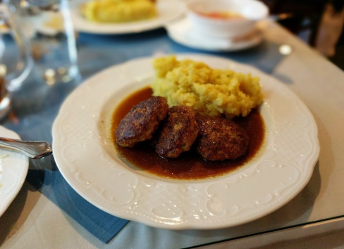 A plate with three meatballs in sauce, served with a side of yellow mashed plantains.
