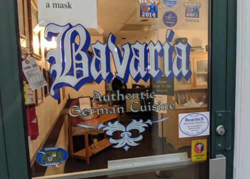 Sign on a door reading "Bavaria - Authentic German Cuisine" with various awards and a mask requirement notice.