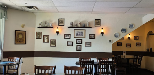 Cozy restaurant interior with wooden tables, framed photos on the walls, and decorative plates. Warm lighting enhances ambiance.