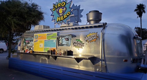 A silver food truck named "Gyro Hero" with a colorful menu, parked under a twilight sky.