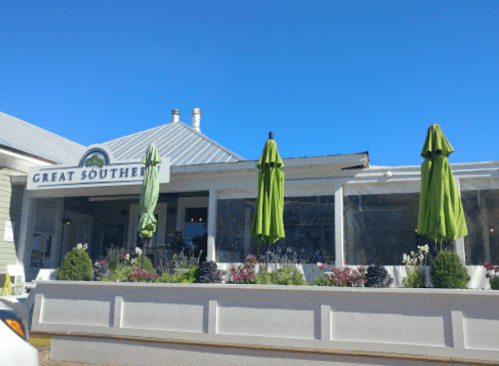 A restaurant named "Great Southern" with green umbrellas outside, surrounded by flowers and a clear blue sky.