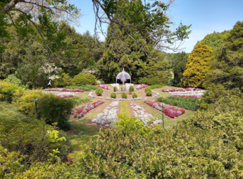 A vibrant garden with colorful flower beds arranged around a central gazebo, surrounded by lush greenery.