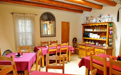 Cozy dining area with wooden tables and chairs, red tablecloths, and a rustic wooden sideboard. Natural light from a window.