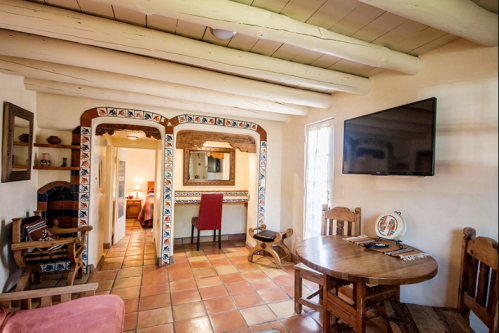 Cozy interior of a rustic room with wooden beams, a dining table, and a TV, featuring warm tile flooring.