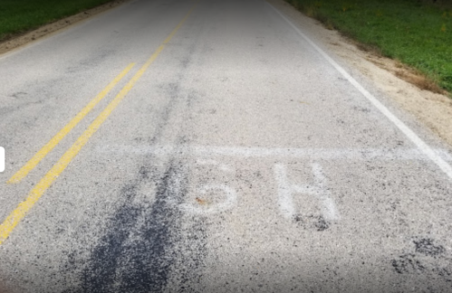 A view of a rural road with yellow lane markings and white spray-painted numbers on the pavement.