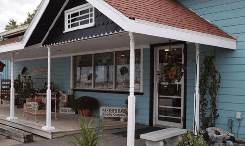A charming blue building with a porch, featuring a sign and decorative plants, inviting visitors inside.