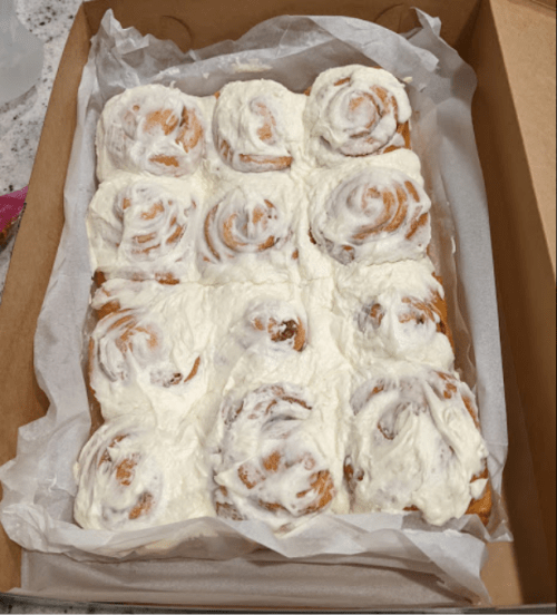 A box of freshly baked cinnamon rolls topped with creamy frosting, arranged in a neat grid.