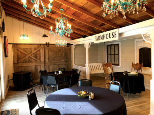A cozy farmhouse interior with tables set for dining, chandeliers, and rustic decor.