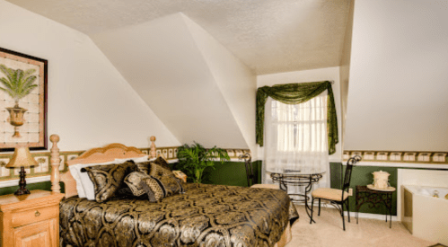 Cozy bedroom with a sloped ceiling, featuring a bed, decorative plants, and a small seating area.