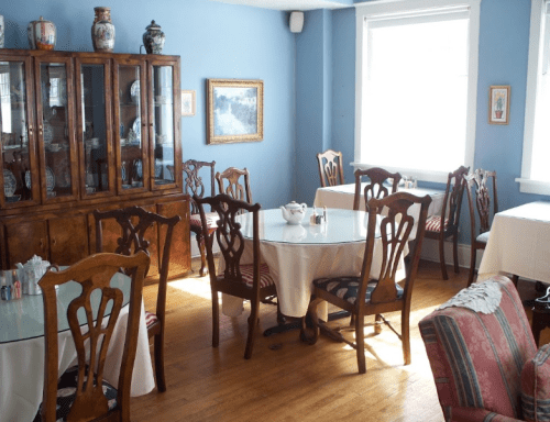 Cozy dining room with wooden furniture, tables covered in white cloths, and blue walls adorned with artwork.