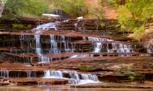 A serene waterfall cascading over layered rock formations, surrounded by lush greenery.